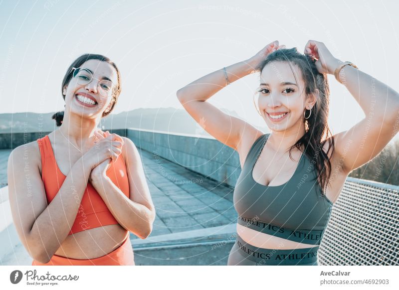 Zwei Frauen binden sich die Haare zusammen, bevor sie im Freien auf einem städtischen Platz joggen. Training Gewicht verlieren mit Freunden zusammen lächelnd in die Kamera glücklich. Afrikanische arabische Menschen tun Übung.