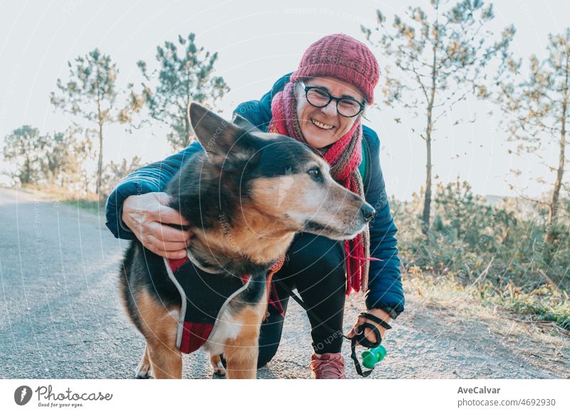 Alte Frau mit seinem Hund bei einem Spaziergang Porträt trägt einen Hut für Frühling und Winter lächelnd toc amera. Ältere Menschen geistige Gesundheit Aktivitäten im Freien, Aktiver Lebensstil im dritten Alter. Glückliche Oma