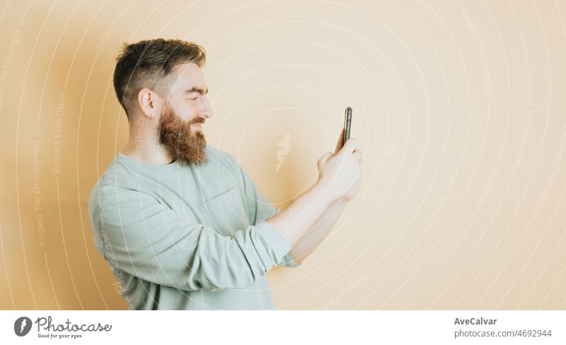 Junger Mann bärtigen Hipster-Stil hält ein Mobiltelefon und ein Foto, gelben Hintergrund. Emotion über den Erhalt einer guten neuen, abnehmbaren Hintergrund mit Kopie Raum. Junge Menschen soziales Netzwerk