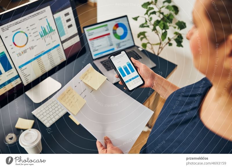 Geschäftsfrau arbeitet mit Finanzdaten in Diagrammen und Tabellen auf Smartphone und Computer. Unternehmerin schaut sich Verkaufsstatistiken an Business Büro