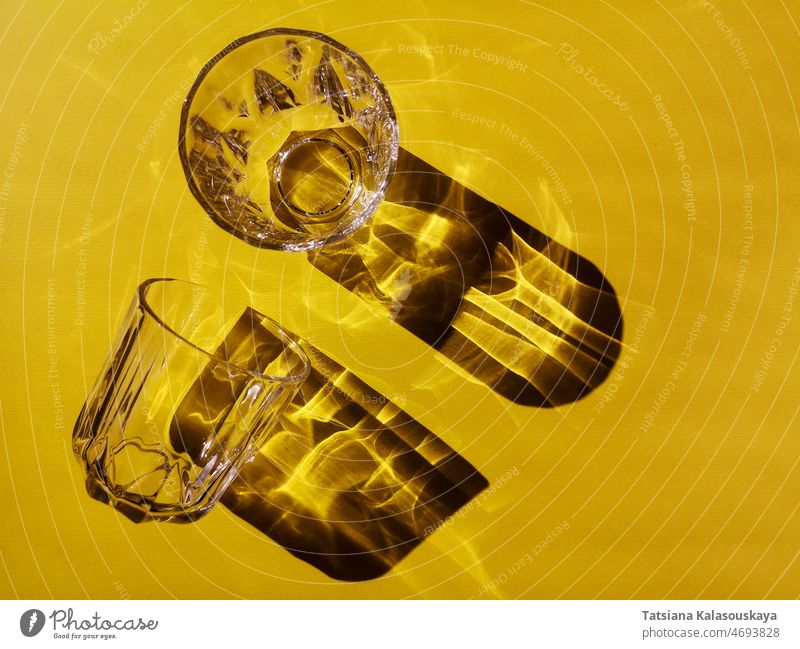 Zwei Glasgläser auf einem gelben Hintergrund in hartem Licht mit Schatten durchsichtig übersichtlich Brille Tasse Gerichte Getränke Durst Wasser trinken