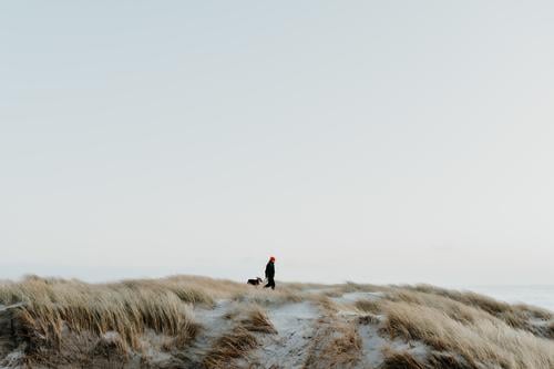 Mann mit Hund in den Dünen Winter Spaziergang Abend Abendstimmung rote mütze ruhig einsam Ferien & Urlaub & Reisen Küste Sand Strand Meer Natur Erholung