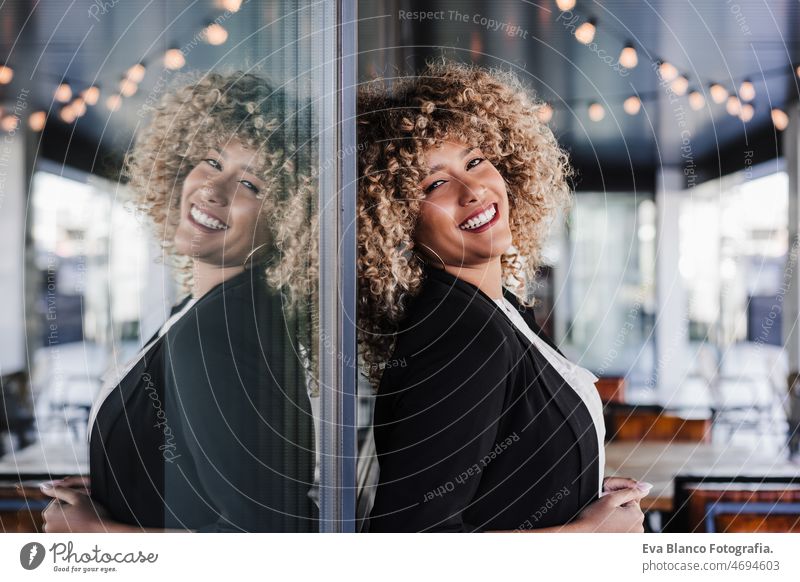 Porträt einer schönen lächelnden Geschäftsfrau, die sich in einem Café an ein Glas lehnt, Geschäftskonzept Afro-Look hispanisch Handy Großstadt Wolkenkratzer