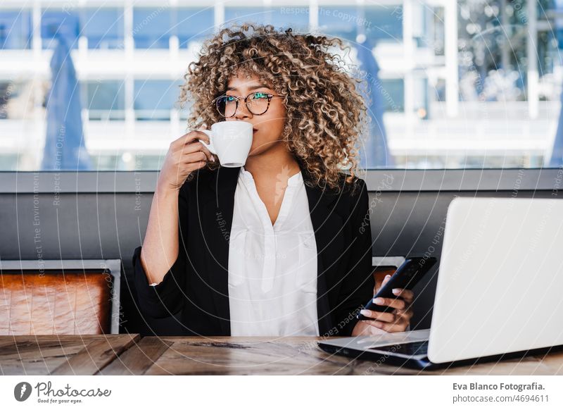 schöne hispanische Afro-Geschäftsfrau mit Brille in einem Café, die an einem Laptop und einem Handy arbeitet Computer Afro-Look Frau Business arbeiten