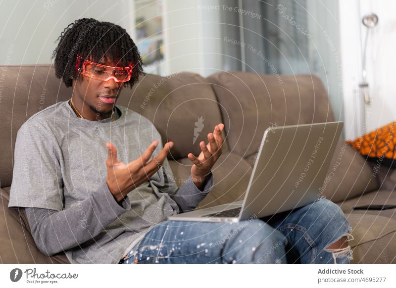 Schwarzer Mann mit futuristischer Brille schaut auf Hände Cyberpunk Zukunft Hochtechnologie trendy modern Laptop Wohnzimmer Licht männlich schwarz