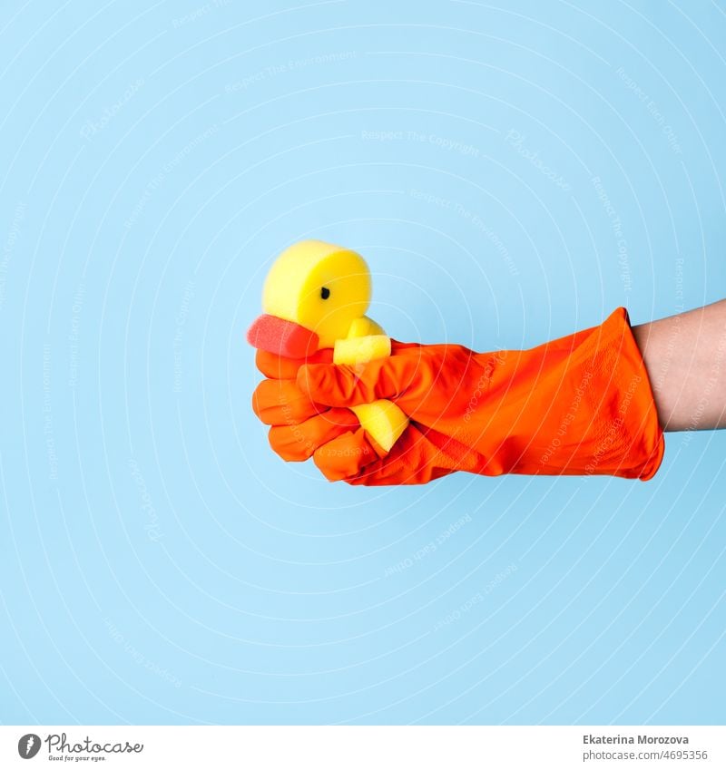 Hand in orangefarbenen Gummihandschuhen hält einen Waschschwamm gelbe Ente. Blauer Hintergrund. Housekeeping und Reinigung Service-Konzept. Frühling Zeit saisonale Reinigung kreativ, Flyer