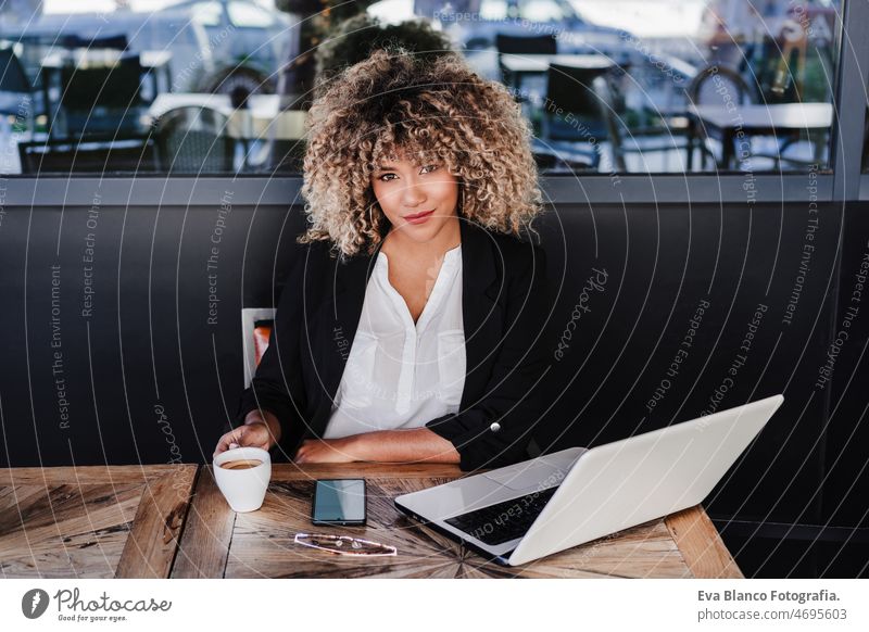 Selbstbewusste hispanische afroamerikanische Geschäftsfrau in einem Café, die an einem Laptop und einem Mobiltelefon arbeitet.business,lifestyle Computer