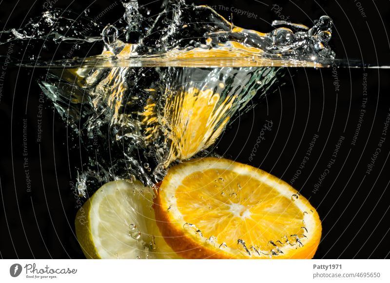 Unterwasseraufnahme von ins Wasser fallenden Orangen- u. Zitronenscheibe. splash Wasserspritzer frisch Nahaufnahme Obst spritzen nass Highspeed Detailaufnahme