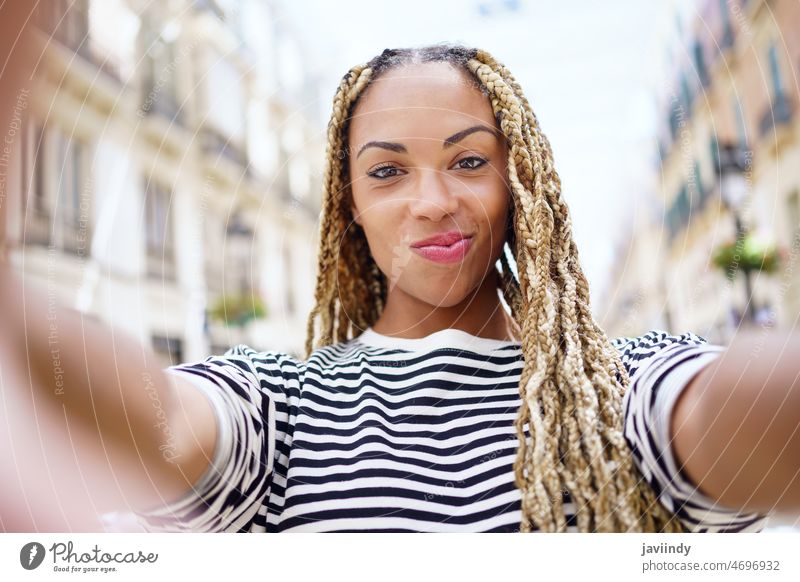Schwarze Frau mit Afrozöpfen, die in einer städtischen Straße ein Selfie mit einem Smartphone macht. Selbst Porträt schwarz Zopf afrobraid Rastalocken Glück