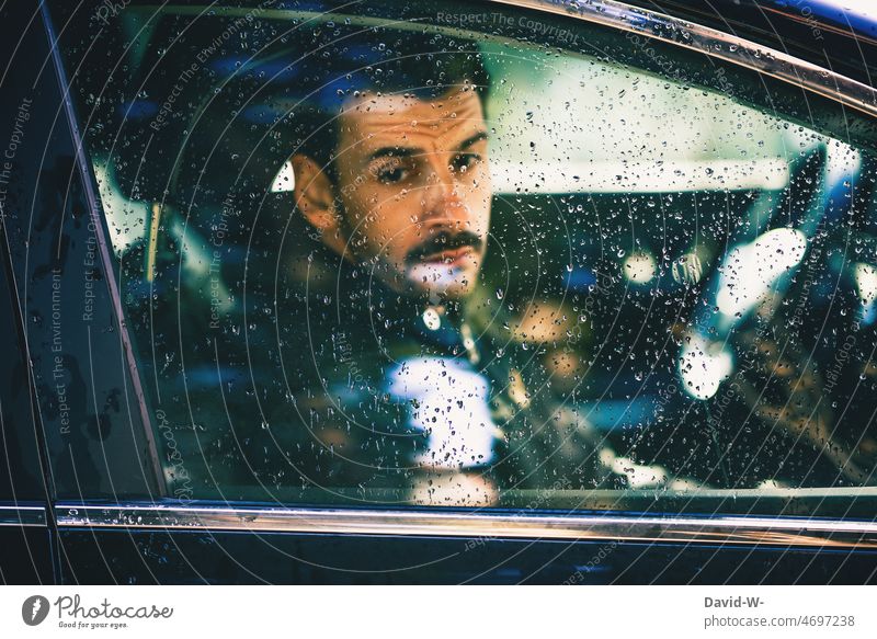 Mann schaut bei Regenwetter deprimiert aus dem Auto sitzen Autoscheibe Regentropfen Fensterscheibe schlechtes Wetter depressiv genervt Reflexion & Spiegelung