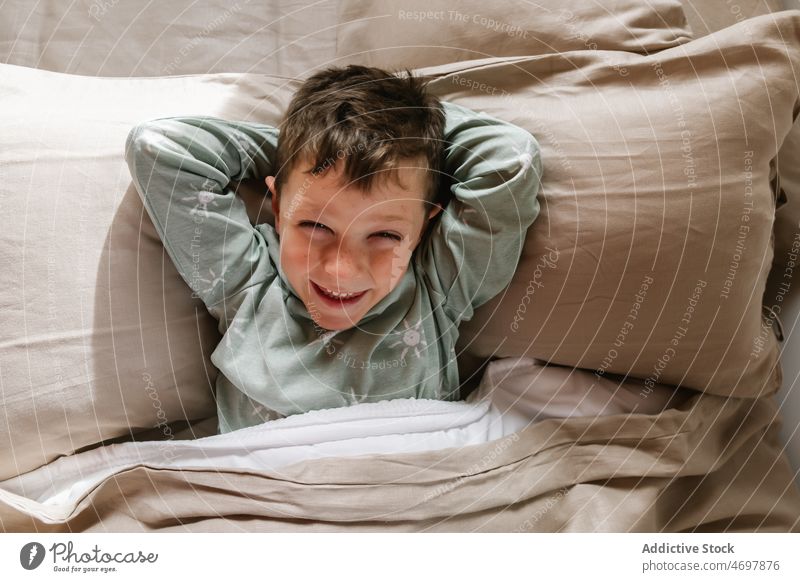 Fröhlicher Junge auf dem Bett liegend Kind Fenster Schlafzimmer Pyjama Kindheit Morgen heiter Spaß haben lustig Appartement bezaubernd flach Freude niedlich