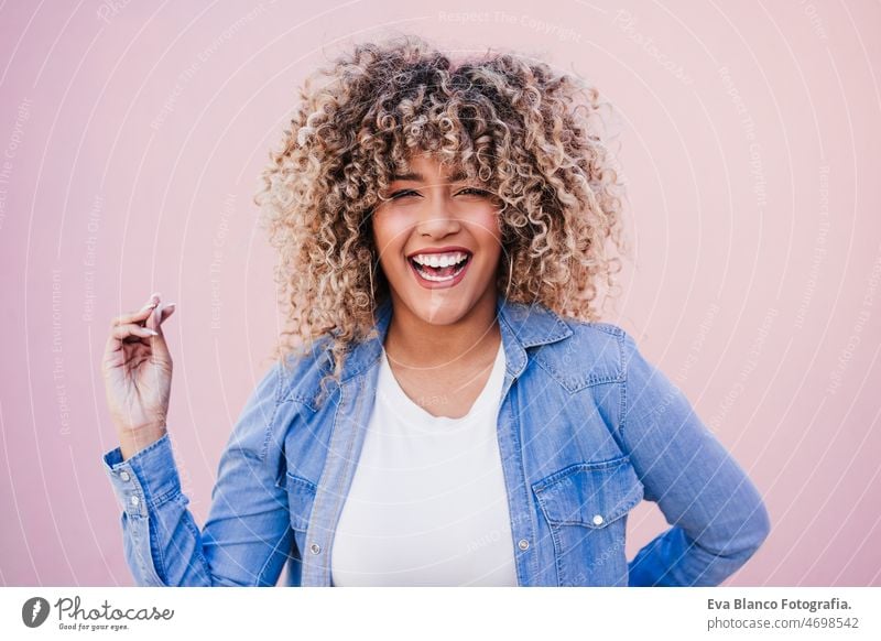 Porträt einer lächelnden hispanischen Frau mit Afro-Haar in der Stadt im Frühling. Urbaner Lebensstil Afro-Look Glück Lächeln Großstadt rosa Freizeitkleidung