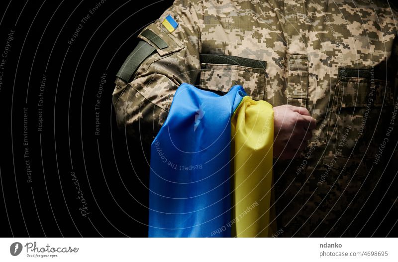 Ein ukrainischer Soldat hält eine Flagge des unabhängigen Staates Ukraine. Standhaftigkeit und Mut des Volkes im Kampf gegen die Invasoren. Der ungebrochene Geist der Nation. Symbol der Unabhängigkeit