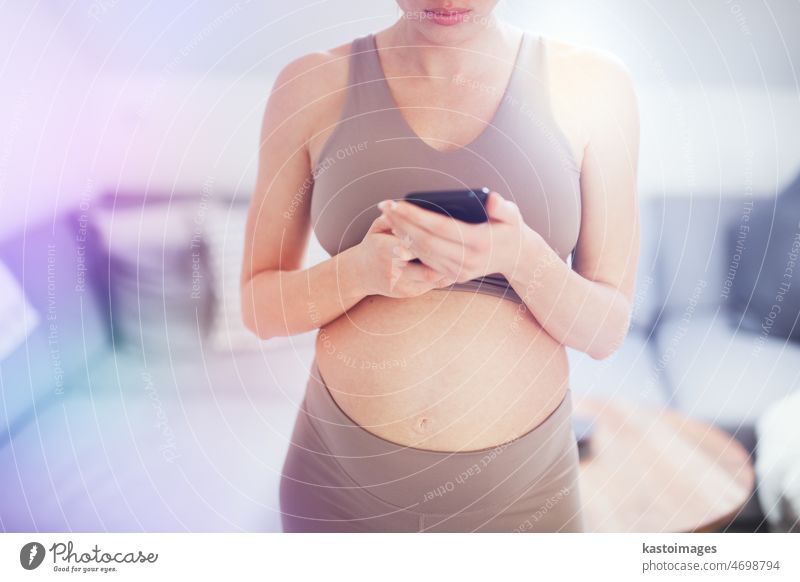 Nahaufnahme eines schwangeren Frauenbauches. Frau hält und mit Handy-Smartphone-App zu Hause Innenräume. Schwangerschaft, Technologie, Online-Shopping, Vorbereitung und Erwartung Konzept.