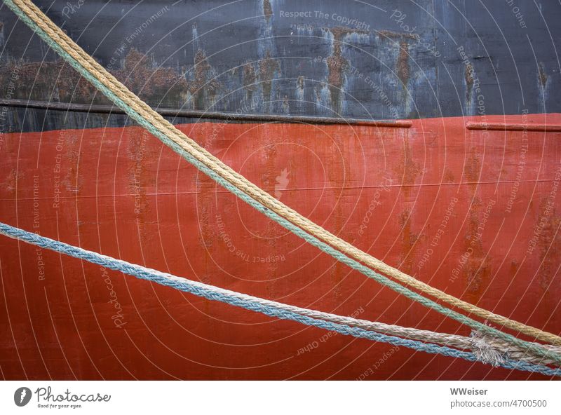 Taue hängen vor der Wand eines riesigen Schiffes quer durch das Bild Diagonal rot abstrakt maritim Wasserfahrzeug Seil Rost Farben farbig Anstrich Material