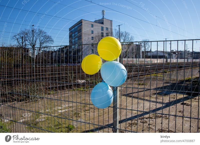 Luftballons in den Farben der Ukraine an einem Zaun an einer tristen Bahntrasse. Landesfarben Friedenstaube Friedensbotschaft Krieg Angriffskrieg