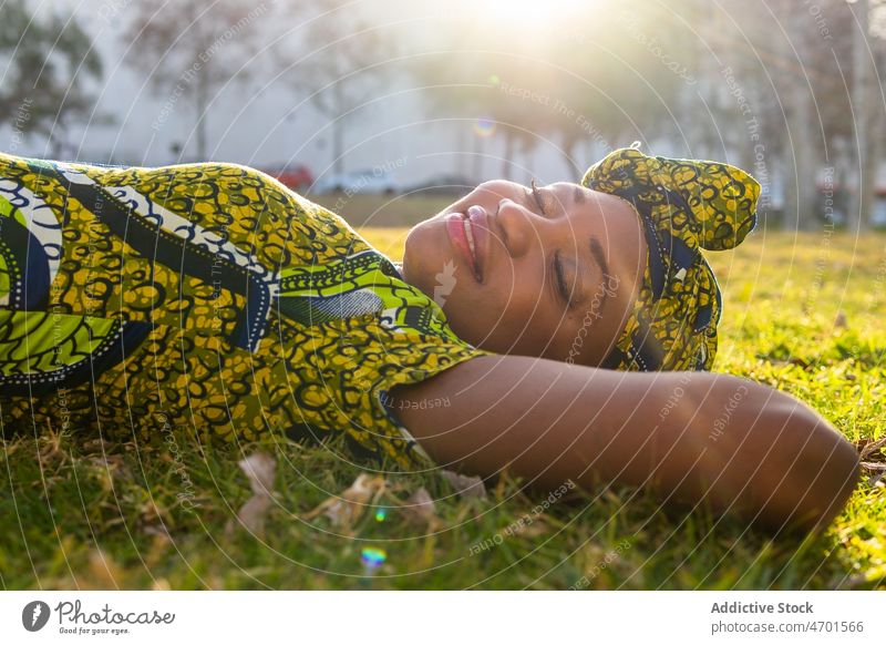 Afrikanische Frau auf dem Rasen ruhend Park Lächeln Wochenende Sommer froh Gras tagsüber Tradition Kopftuch Porträt Afroamerikaner schwarz ethnisch Glück