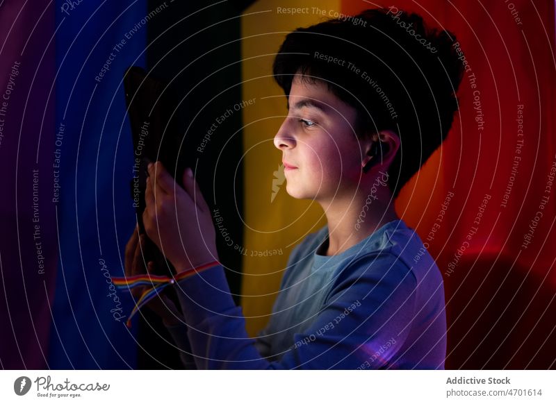 Ethnischer Junge schaut Video auf Tablet gegen LGBT-Flagge zuschauen Tablette benutzend Drahtlos Ohrstöpsel digital dunkel lgbtq Fahne nicht binär Apparatur