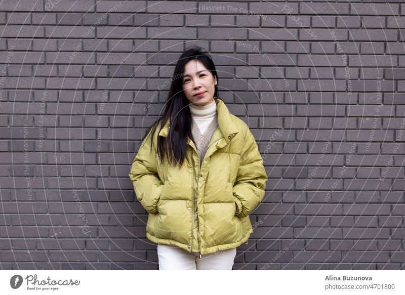 Candid Lifestyle-Porträt von Stylish Junge asiatische schöne Frau stehend im Freien in der Nähe von grauen Backsteinmauer im Frühjahr oder Herbst Saison.