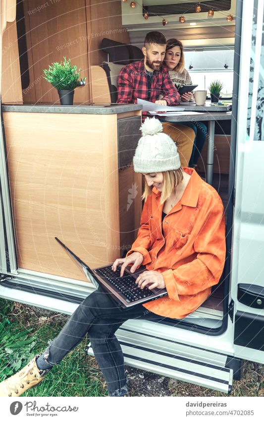 Frau bei Telearbeit in der Tür eines Wohnmobils sitzend Lächeln Technik & Technologie Laptop Tablette Kleintransporter Fernarbeit Sitzen Ausflug Menschen