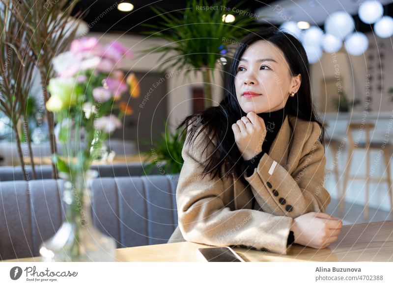 Traurige müde asiatische Frau einsam in einem Café während der Quarantäne zur Selbstisolierung für COVID-19 Coronavirus soziale Distanzierung Prävention. Psychische Gesundheit, Angst deprimiert Denken Dame.