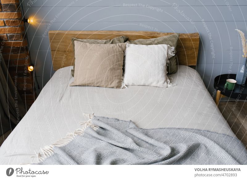 Ein modernes, skandinavisches, graues Schlafzimmer mit pastellfarbener Bettwäsche und Kissen. Bett aus Holz Möbel Kopfkissen Appartement Design Haus Inspiration