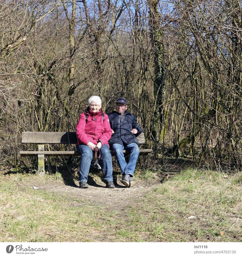 Seniorenpaar genießt die erste Frühlingssonne Sonne Sonnenschein Mann Frau Hobby Fotografin sitzen genießen zusammen Holzbank draußen geschützt kahle Bäume