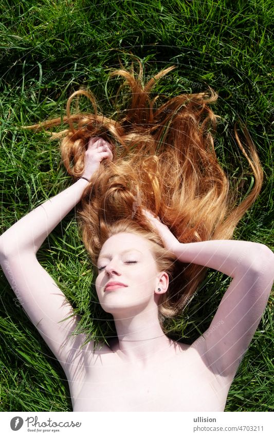 Porträt einer schönen jungen sexy rothaarigen Frau, die ihre Arme hebt und in der Frühlingssonne auf dem grünen Gras liegt Lügen hebt die Arme rote Haare