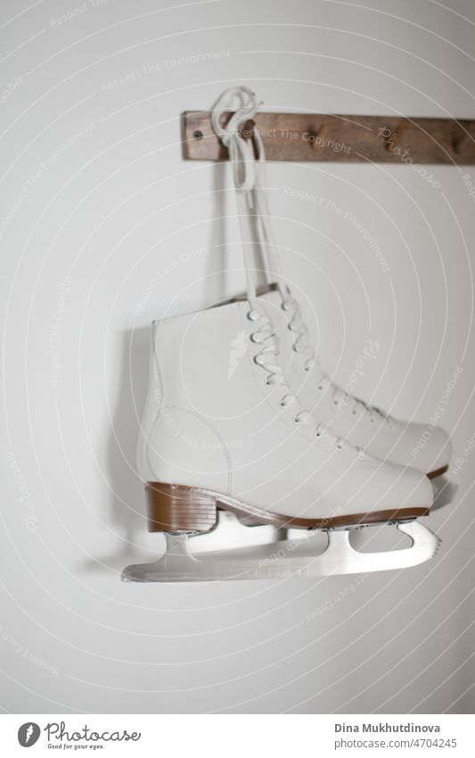 Weiße Schlittschuhe hängen an weißen Schnürsenkeln an einem hölzernen Aufhänger an einer weißen Wand. Winter aktiv Sport Figur Schlittschuhlaufen Ausrüstung.