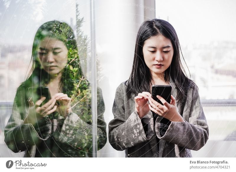 Chinesische Geschäftsfrau, die ein Mobiltelefon im Büro benutzt. Reflexion auf Glas asiatisch Frau Laptop Technik & Technologie Café Kaffee Kantine Tablette