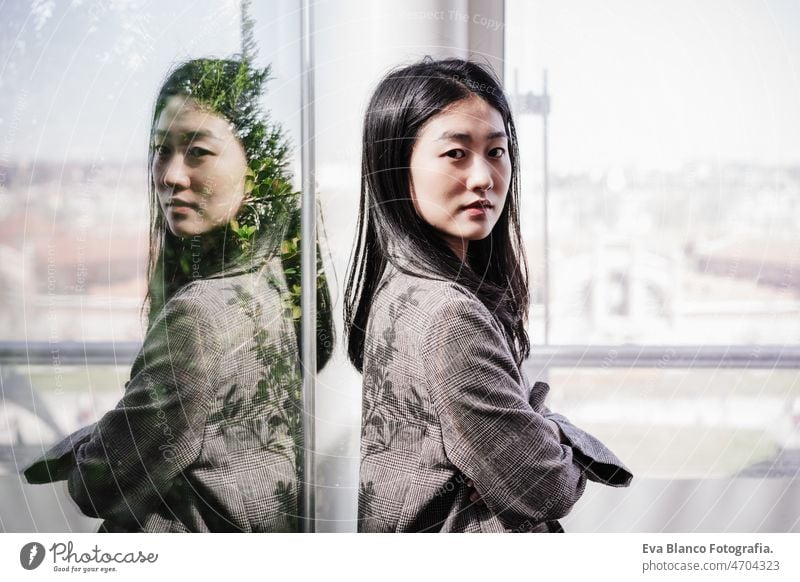 Porträt einer selbstbewussten chinesischen Geschäftsfrau mit verschränkten Armen im Büro. Reflexion auf Glas Chinesisch asiatisch Frau Laptop