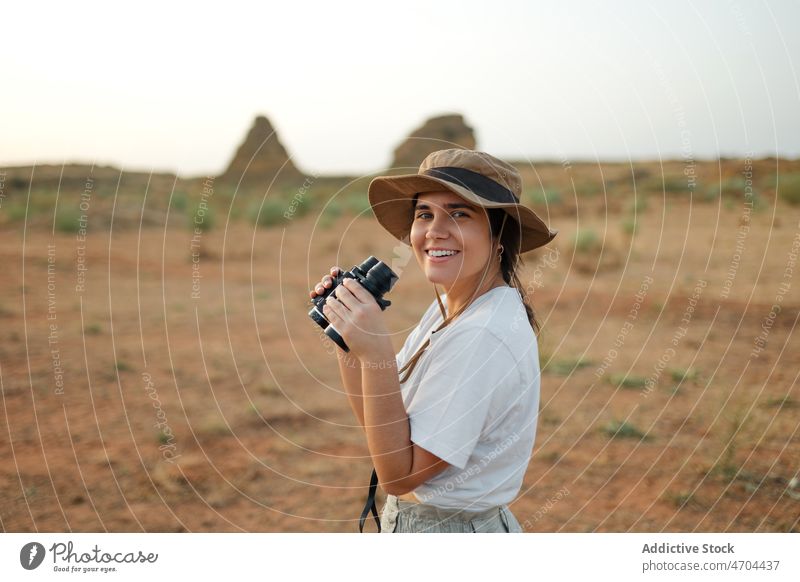 Lächelnde Frau schaut durch ein Fernglas in der Wüste Reisender Ausflug Abenteuer wüst trocken erkunden beobachten Interesse neugierig unfruchtbar trocknen