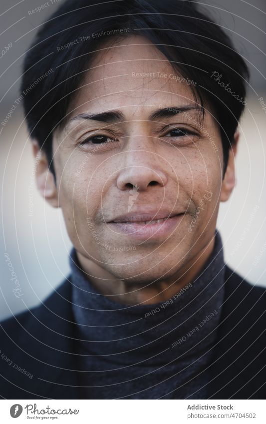 Lächelnder ethnischer Mann mit schwarzen Haaren und Rollkragenpulli positiv Vorschein Stil Porträt Individualität Persönlichkeit Haarschnitt Jacke heiter