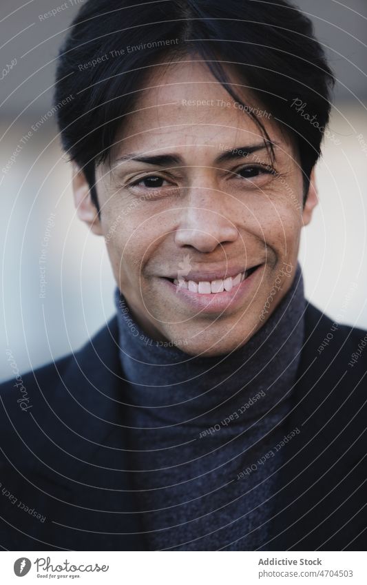 Lächelnder ethnischer Mann mit schwarzen Haaren und Rollkragenpulli positiv Vorschein Stil Porträt Individualität Persönlichkeit Haarschnitt Jacke heiter
