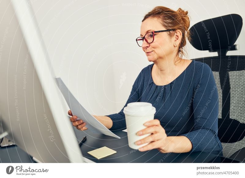 Unternehmerin liest mit Zufriedenheit Finanzdaten. Zufriedene glückliche Geschäftsfrau, die im Büro arbeitet und am Schreibtisch sitzt und einen Computer benutzt