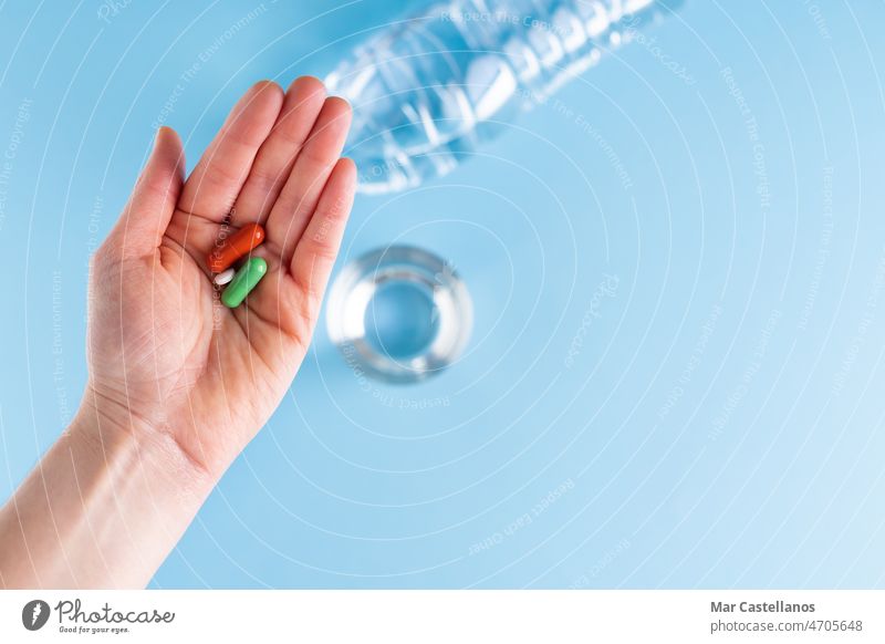 Hand zeigt drei Pillen mit Flasche und Glas Wasser auf blauem Hintergrund. Gesundheit und Medizin Konzept. fangen Blauer Hintergrund Tablette Behandlung
