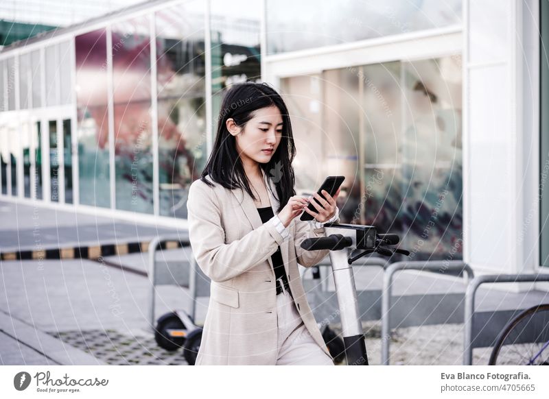Selbstbewusste Geschäftsfrau entriegelt Elektroroller per Smartphone auf der Straße. nachhaltiger Verkehr Chinesisch Frau elektrisch Tretroller Kopfhörer Musik