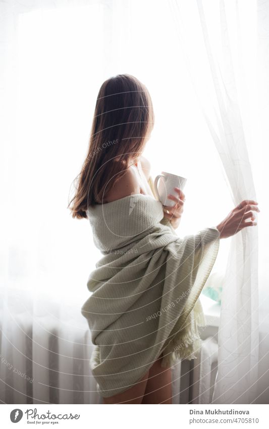 Junge schöne brünette Frau von hinten in kuscheligen Decke am Morgen in ihrem Haus. Wohnung leben Millennial Lebensstil trinken Kaffee. Komfort bequem Café