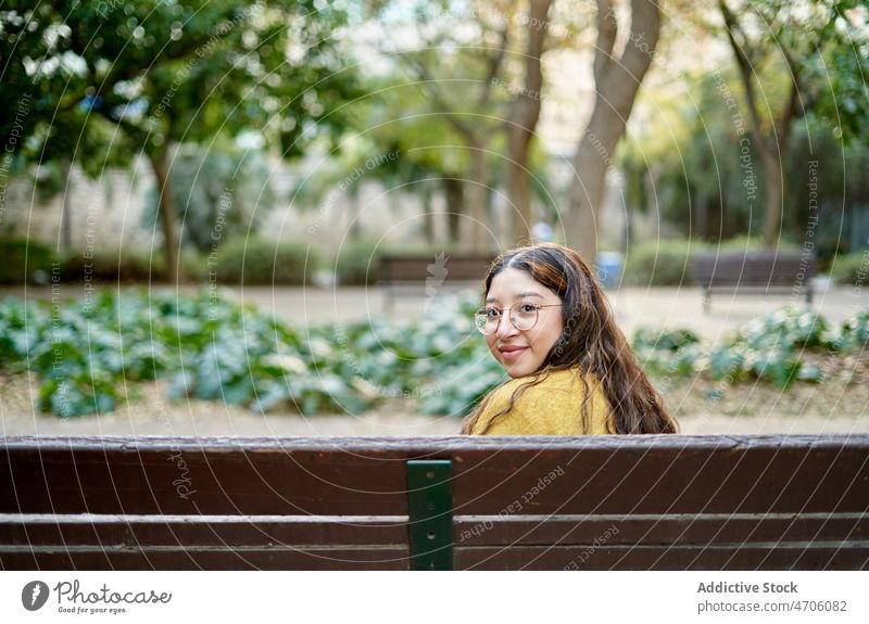 Positive Frau auf einer Bank sitzend Park Vorschein feminin Stil ruhen Pflanze Freizeit Zeitvertreib jung Lächeln Sommer Brille Dame lange Haare Jugend schön