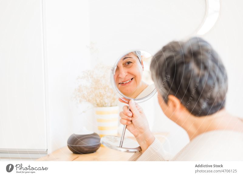 Frau betrachtet den Spiegel im Zimmer Reflexion & Spiegelung Vorschein Hautpflege Lebensmitte heimisch feminin täglich Routine Raum Bademantel heimwärts Inhalt
