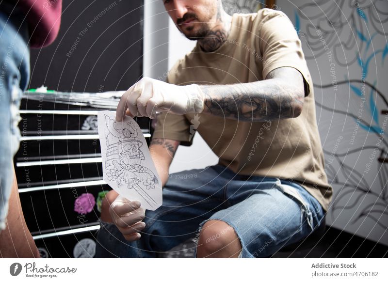Unbekannter Tätowierer zeigt Skizze an gesichtslosen Kunden Klient Tattoo Design transferieren Meister Salon Arbeit Tiefgang Atelier professionell Stil Job