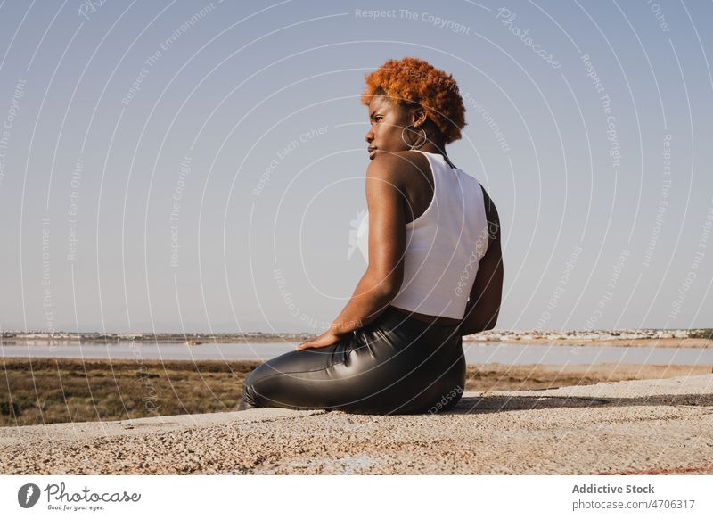 Schwarze Frau sitzt am Ufer des Meeres in sonnigen Tag ruhen trendy Stil Sand Sommer MEER nachdenklich Individualität Hose sitzen ruhig sich[Akk] entspannen