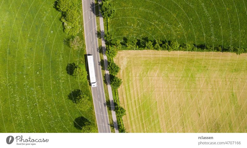 Luftaufnahme einer zweispurigen Straße durch eine ländliche Gegend und bewirtschaftete Felder mit einem weißen LKW. Drohnenaufnahme und Kopierraum für Text