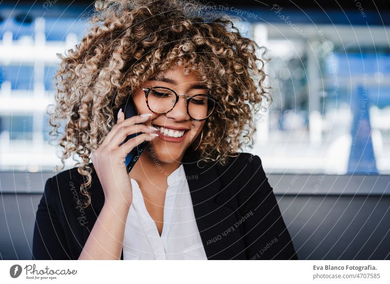Lächelnde hispanische afroamerikanische Geschäftsfrau in einem Café, die an einem Laptop und einem Mobiltelefon arbeitet. Computer Afro-Look Frau Business