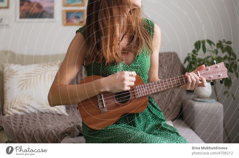 Junge brünette Frau in grünem Kleid spielt Ukulele zu Hause. Wohnung leben. Musikalisch begabte Person spielt kleine Gitarre als Hobby oder Beruf. schön