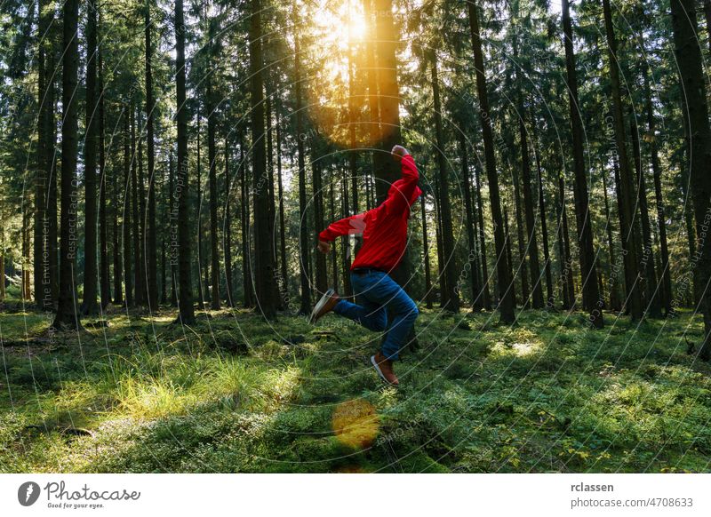 Junger Mann springt im grünen Wald mit roter Jacke und genießt die Natur Wanderer erkunden Stille springen Herbst Abenteuer analog Frühling Sommer laufen schön