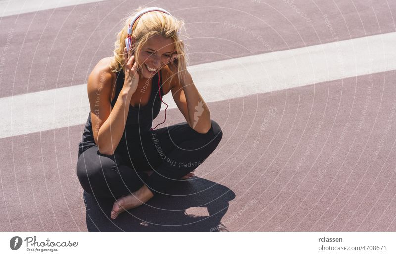 Junge Frau hört Musik mit Kopfhörern zur Fitnessmotivation. Porträt einer lächelnden jungen Frau in Sportkleidung, die entspannt sitzt und sich inspirieren lässt.
