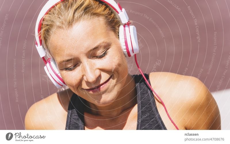 Junge Frau hört Musik mit Kopfhörern zur Fitnessmotivation. Porträt einer jungen Frau in Sportkleidung, die entspannt sitzt und sich inspirieren lässt. passen