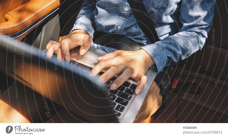 Geschäftsfrau tippt auf ihrem Laptop auf dem Rücksitz einer Luxuslimousine. PKW Geschäftsreisen Chauffeur Dienst beschäftigt Job Mitteilung Limousine Reichtum