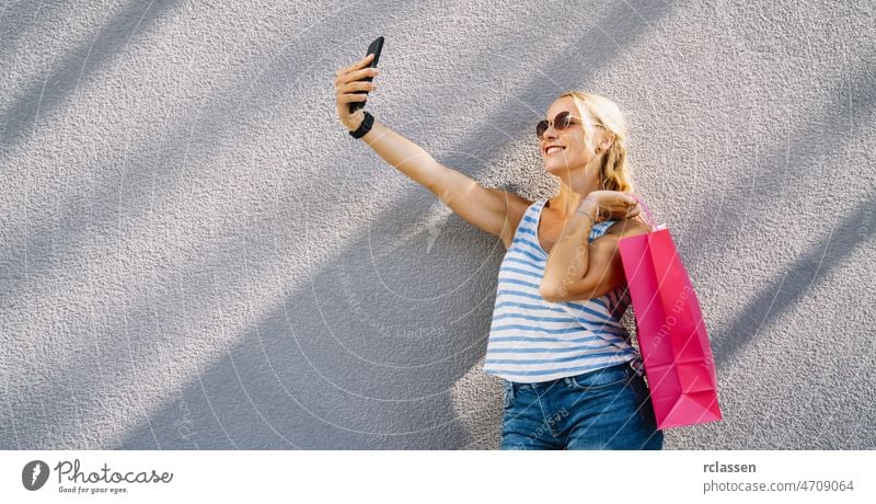 Junge attraktive Frau, die Selfie mit Smartphone mit Einkaufstasche nach dem Einkaufen. hält Handy und tun Selfie. Mode Sommer 20s Tasche brünett Großstadt